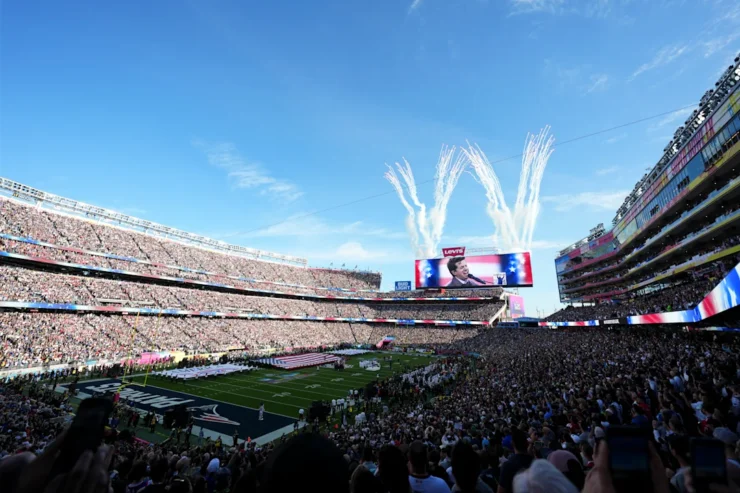 Široki kadar prepunog Levi's stadiona tijekom ceremonije prije početka Super Bowla. Na velikom ekranu prikazan je pjevač, dok se iza ekrana u nebo diže bijeli vatromet. Na terenu su postavljene velike američke zastave, a tribine su ispunjene tisućama gledatelja pod vedrim plavim nebom.